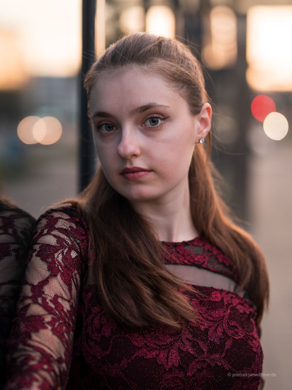 Nahes Portrait einer jungen Frau im weinroten Spitzenkleid vor abendlichen Lichtern der Stadt