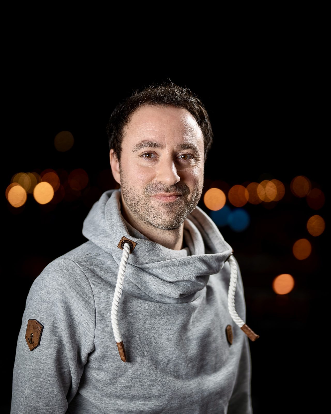 Jan Wittmer in grauem Kapuzenpullover vor unscharfen nächtlichen Stadtlichtern
