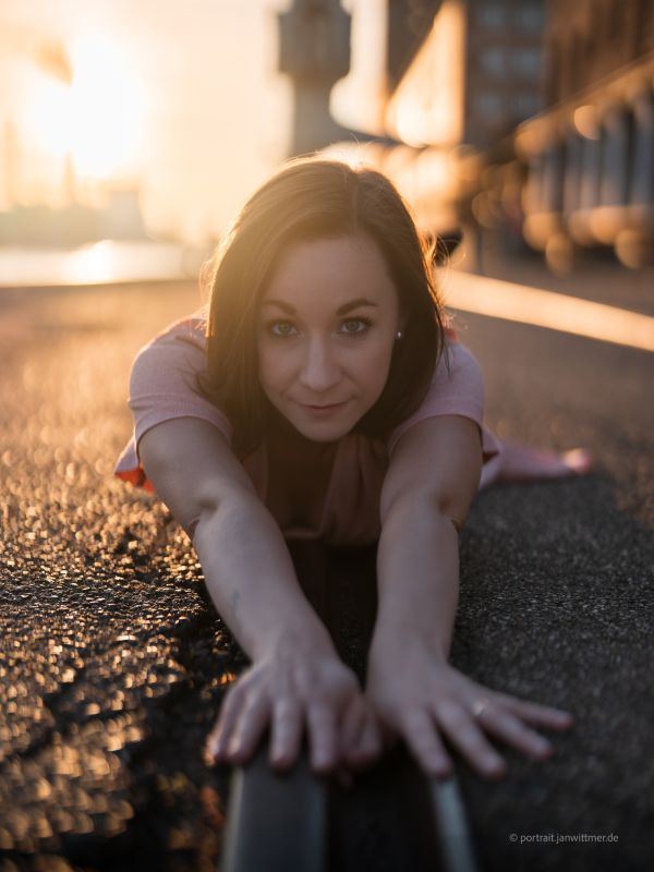 Frau in rosa Bluse liegt auf dem Asphalt und streckt die Hände zur Kamera, Abendsonne im Hintergrund