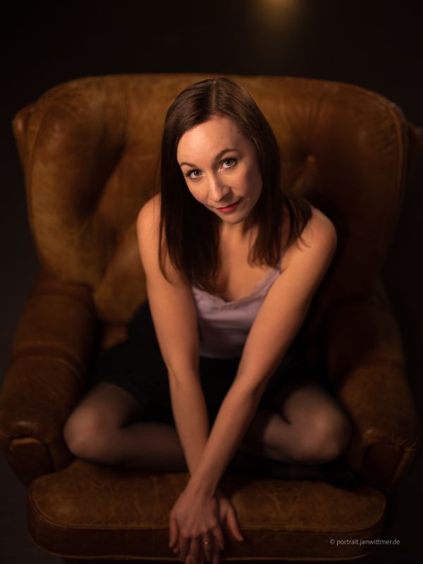 Dunkelhaarige Frau in hellem Top sitzt in einem braunen Ledersessel, von schräg oben fotografiert